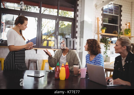 Young man sitting with friends ordering food to waitress at cafe Stock Photo