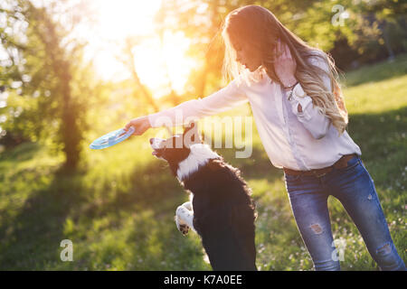 Beautiful brunette playing with dog  in nature during sunset Stock Photo