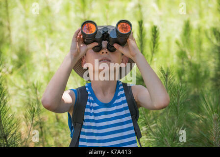 Boy looking through binoculars in woods Stock Photo