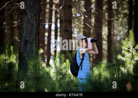 Boy looking through binoculars in woods Stock Photo