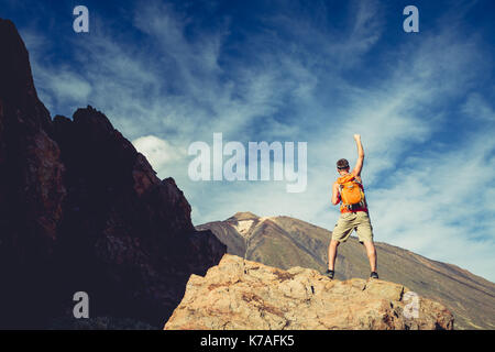 Man with arms outstretched celebrating beautiful inspiring view in mountains. Male hiker or climber with hands up enjoy inspirational landscape on roc Stock Photo