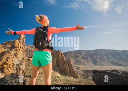 Woman hiker with arms outstretched in mountains. Beauty female runner, hands up and enjoy inspirational landscape on rocky trail footpath on Tenerife, Stock Photo