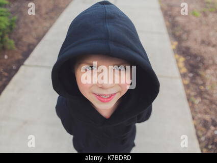 High angle portrait of happy boy wearing black hooded jacket while standing on footpath Stock Photo