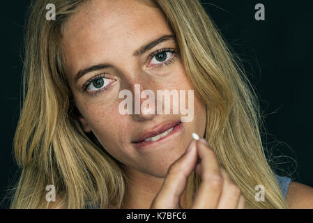 Young woman holding pill and biting lips Stock Photo