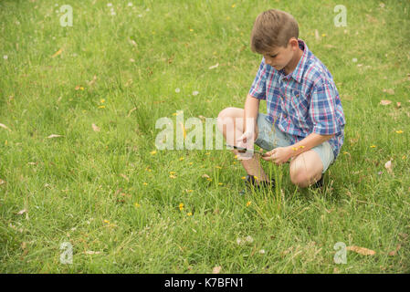 Boy crouching in grass, using digital tablet Stock Photo