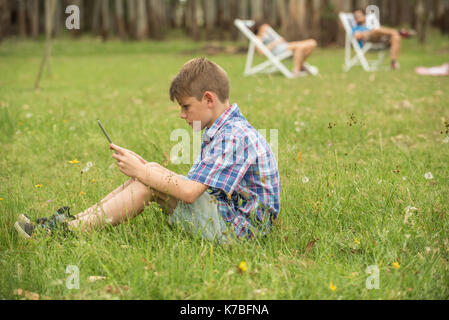 Boy sitting on lawn looking at digital tablet Stock Photo