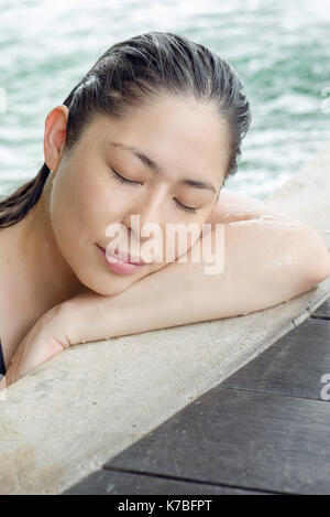 Woman at side of swimming pool resting head on arms Stock Photo