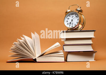 Alarm clock standing on stack of books near open book Stock Photo