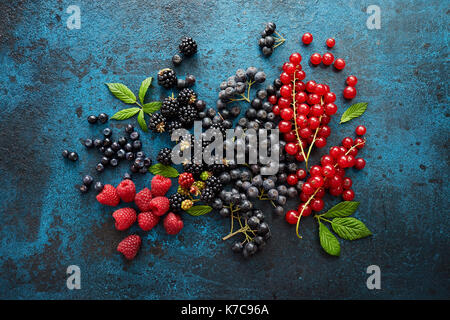 Assorted fresh berries with leaves on metal background. Mix of fresh berries with leaves on textured metal background. Stock Photo