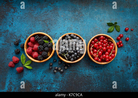 Various summer fruits in a wooden bowls. Assorted fresh berries with leaves on metal background. Stock Photo