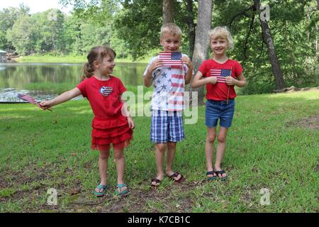 Three happy children waving American flag in patriotic clothes whilst celebration the Fourth of July Stock Photo