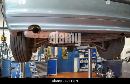 Car up on hydraulic lift at a garage Mechanic working underneath ...