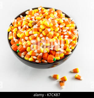 A black bowl over filled with Candy Corn taken on a white background. Stock Photo