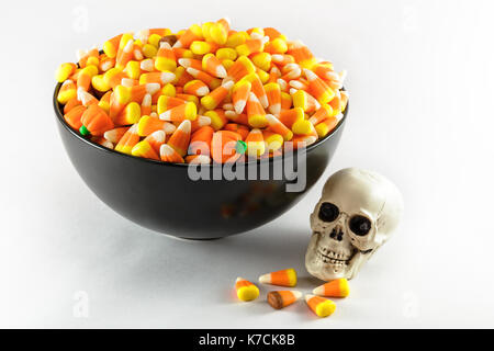 A black bowl over filled with Candy Corn taken on a white background.  A plastic toy skull is also shown in the photo Stock Photo