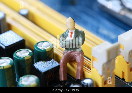 Businessman sit on a computer motherboard in concept of doing business and profiting on technology. Stock Photo