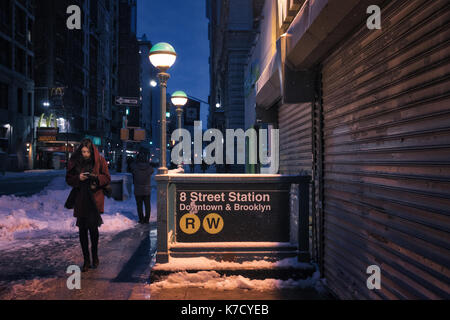 NEW YORK, USA - MARCH 2017 - Subway entrance at 8th street station. An unidentified woman walking in a cold and snowy night. Stock Photo