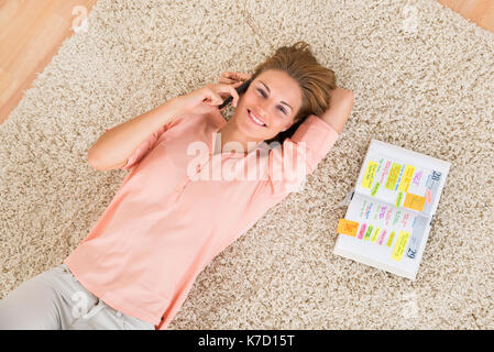 Young Happy Woman Talking On Mobile Phone While Lying On Carpet Stock Photo