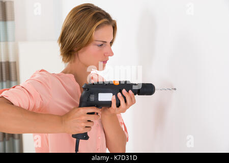 Portrait Of Young Woman Making Hole In Wall With Drill Machine Stock Photo
