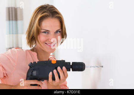 Portrait Of Young Woman Making Hole In Wall With Drill Machine Stock Photo