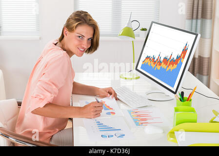 Young Happy Woman Analyzing Financial Statistics In Office Stock Photo