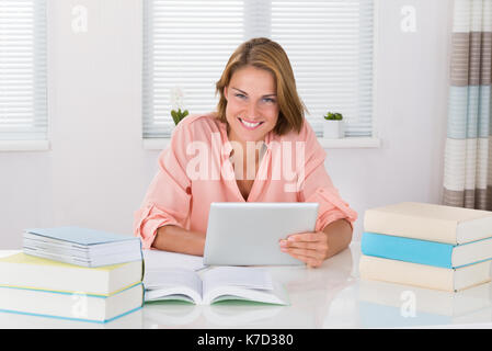 Young Woman With Books Using Digital Tablet At Desk Stock Photo