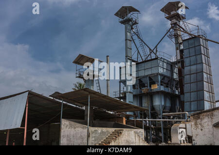 Mysore, India - October 27, 2013: In Ranganathapur, an industrial rice mill shows silos for husks and shafts, ladders and pipes to load them under blu Stock Photo