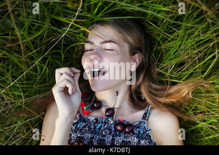 Overhead view of woman eating black cherry while lying on field Stock Photo
