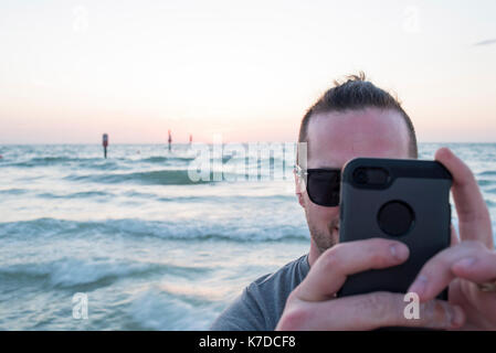 Man photographing through smart phone against seascape during sunset Stock Photo