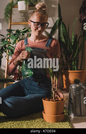 Happy woman watering potted plant at home Stock Photo