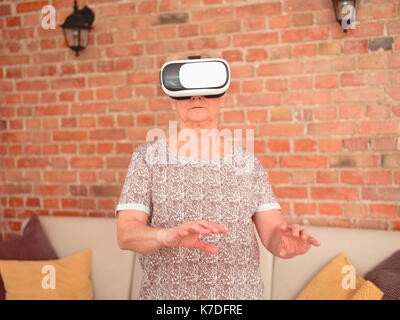 Woman using virtual reality simulator while standing against brick wall at home Stock Photo