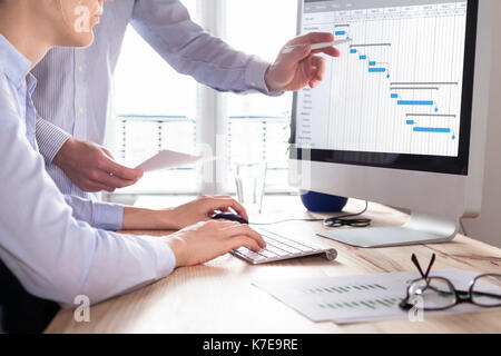 Project management team updating Gantt chart schedule or planning on computer, two business people in office Stock Photo