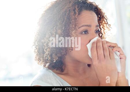 Mid adult woman blowing nose on tissue. Stock Photo