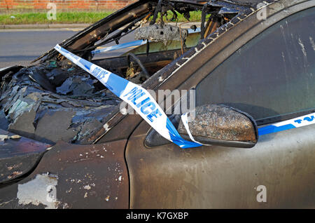 A burnt out car with Police tape on the roadside at Hellesdon, Norfolk, England, United Kingdom. Stock Photo