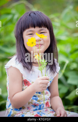 asian children sitting in garden with yellow cosmos flower in hand Stock Photo