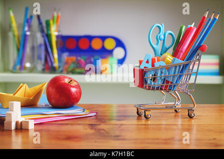 Back to School Shopping Cart with Supplies on Wooden Table. Shopping cart filled with with school necessities. Stock Photo