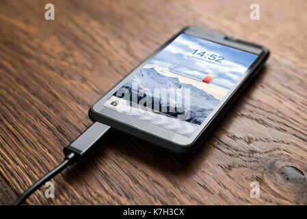 Close-up Of Mobile Phone With Low Battery Symbol On Charge Stock Photo