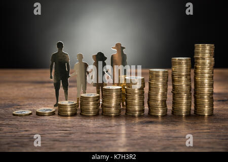 Close-up Of Paper Cutout Family With Stack Of Coins On Wooden Table Stock Photo