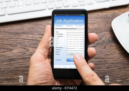 Close-up Of Person Hands Filling Online Job Application On Mobile Phone At Desk Stock Photo