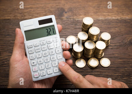 Close-up Of A Businessman Counting Coins Using Calculator Stock Photo