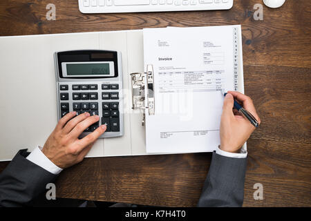High Angle View Of Businessman's Hand Calculating Invoice Using Calculator Stock Photo