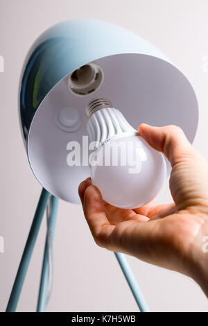 Changing the bulb for led bulb in table lamp in turquoise colours. Stock Photo