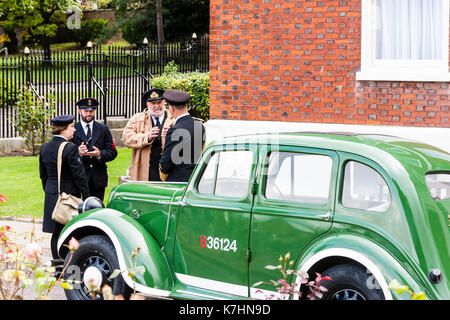 England, Chatham Dockyard. Event, salute to the forties. World war two Royal navy officers and a wren standing in driveway talking together by official bright green vintage car. Stock Photo