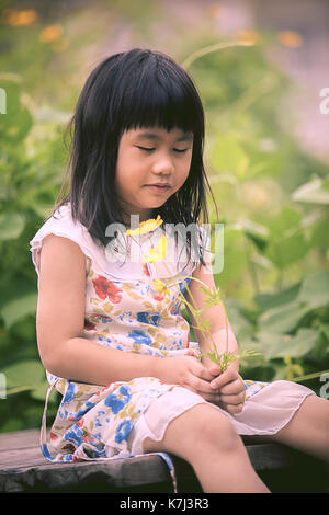 asian children sitting in garden with yellow cosmos flower in hand Stock Photo