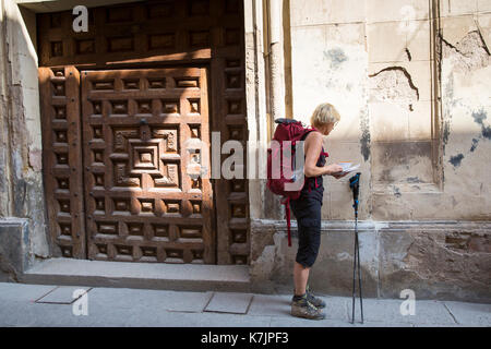 Pilgrim on Camino Santiago de Compostella checking map on route by doorway in Santo Domingo de la Calzada in  La Rioja, Spain Stock Photo