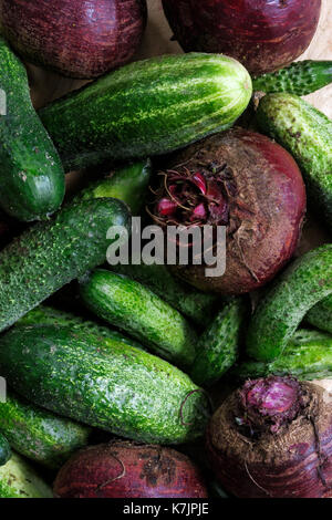 Close up of freshly harvested pickling cucumbers and beetroots on light wooden board from above. Stock Photo