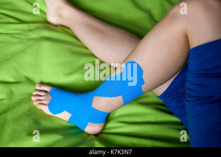 Elastic therapeutic blue tape applied to patient's left leg. Stock Photo