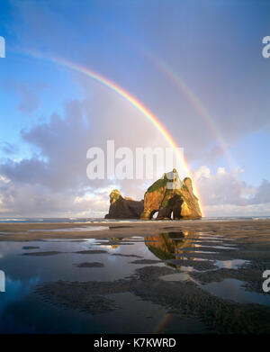 New Zealand. Rainbow over 'Farewell Spit' beach and Rock Arch. South Island. Stock Photo