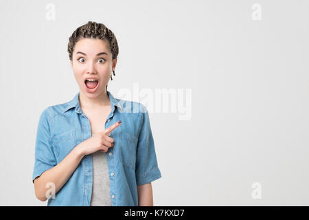 caucasian woman surprise showing product .Beautiful girl with braids pointing to the side Stock Photo
