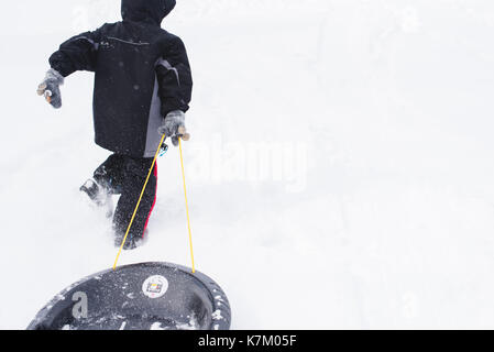 Young boy pulling a sled up a snow covered hill in the winter. Stock Photo