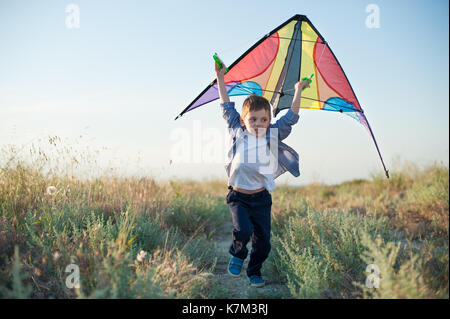 Beautiful boy in shirt running with a kite in hands on the path among field of plants Stock Photo